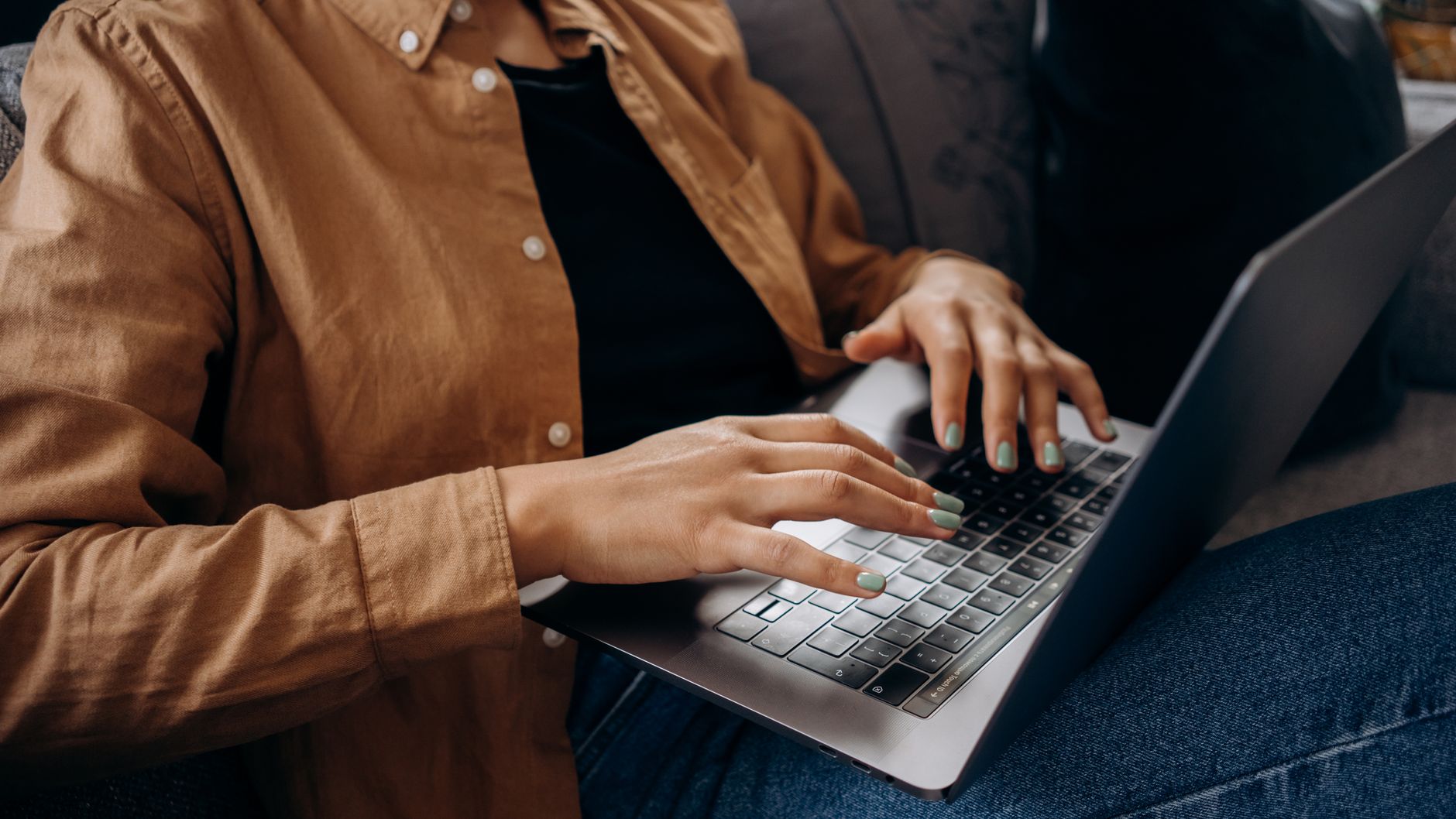 Close-up of an adult typing on a laptop, wearing a brown shirt.