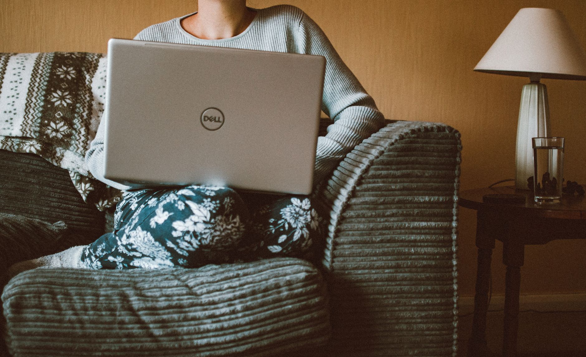 A woman in casual clothing works on a laptop while relaxing on a cozy sofa indoors.